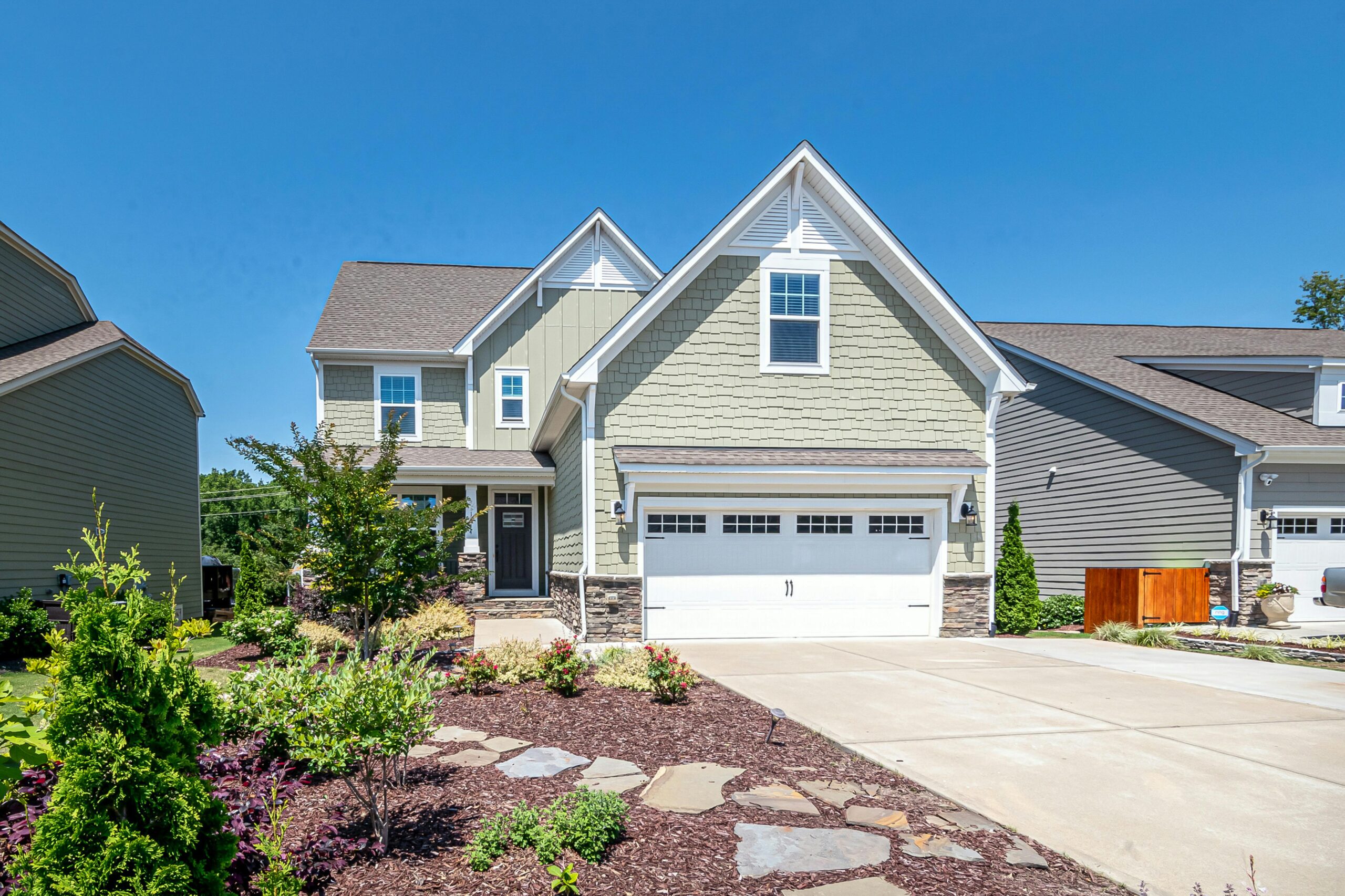 Charming suburban house with green facade, garage, and landscaped yard on a clear day.